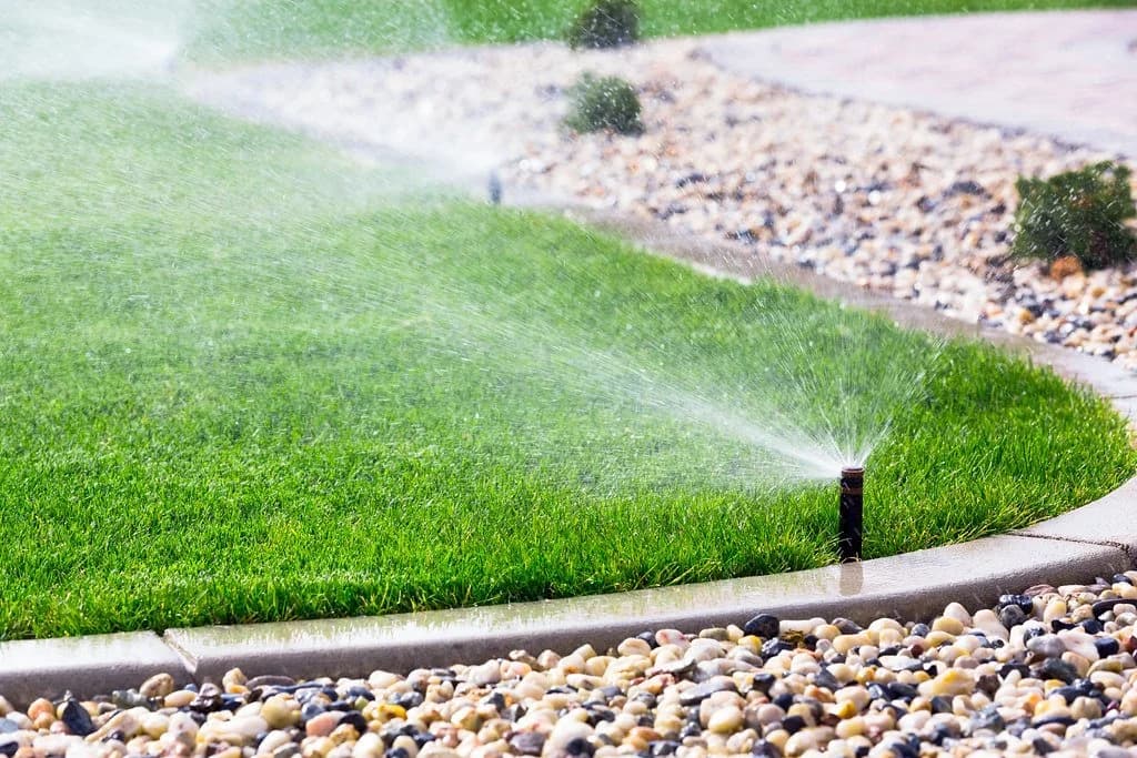 Newly installed irrigation watering a lush green Arizona landscape edged with stone