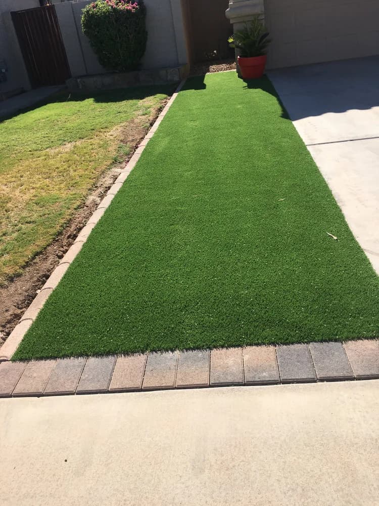Artificial turf strip framed by paver edging beside a driveway